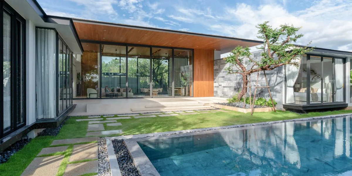 A single-storey Botanica villa with a covered terrace, floor-to-ceiling glazing, a stone garden wall and a private pool in the foreground.