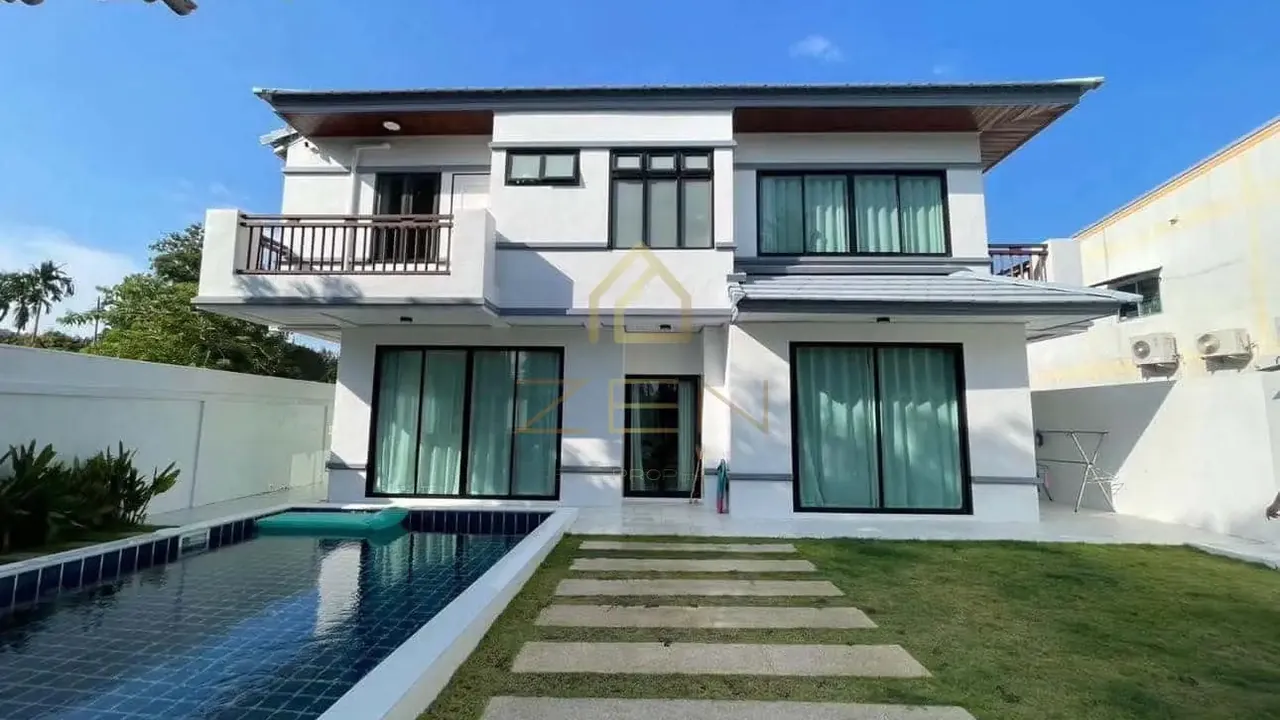 Two-storey white villa with dark window frames behind a lawn, stepping stones and a blue-tiled pool.