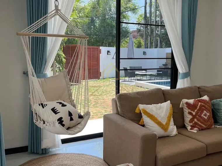 Living room with a hanging chair, a sofa with patterned cushions and a window onto the garden.
