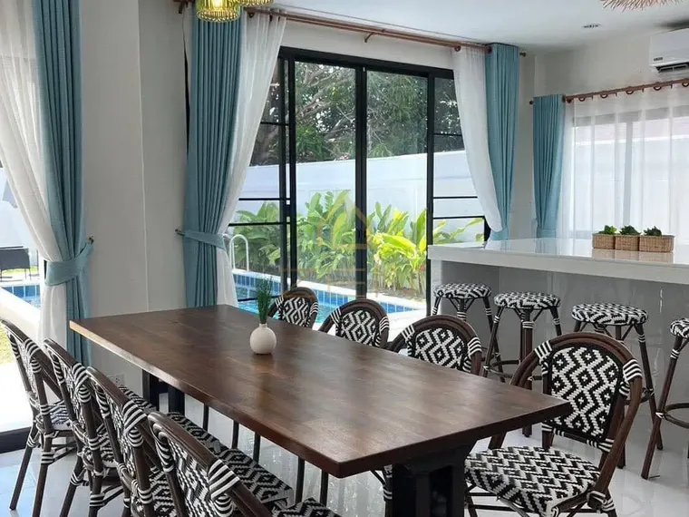 Dining table with patterned chairs beside a kitchen counter and tall windows.