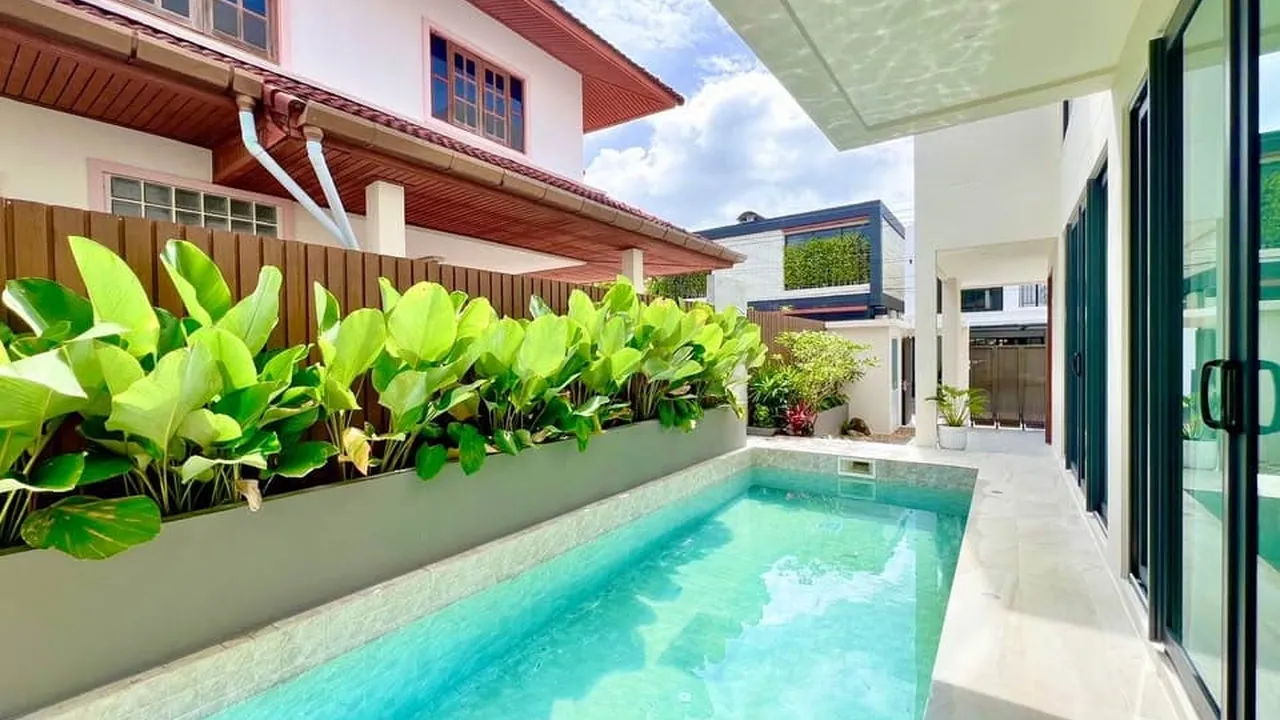 Narrow pool lined with planters along the side of a white two-storey house with sliding glass doors.