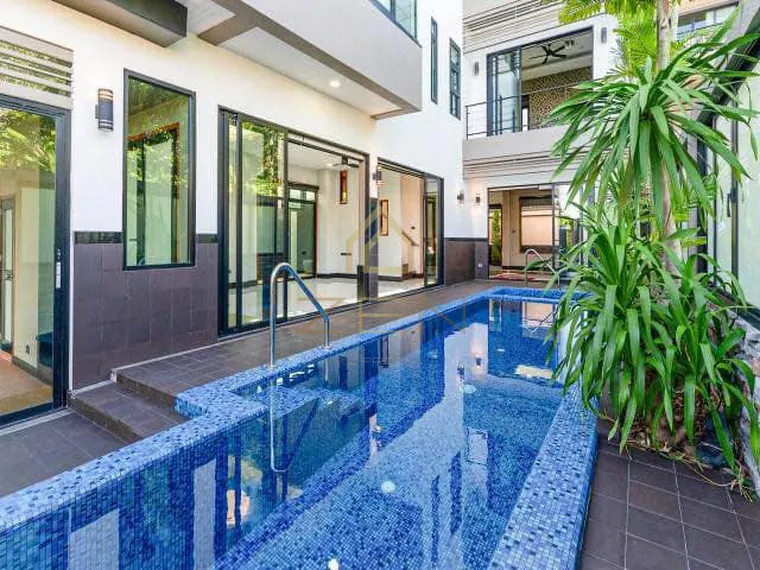 Narrow pool with blue mosaic tiles running beside the house, tropical planting at the far end.