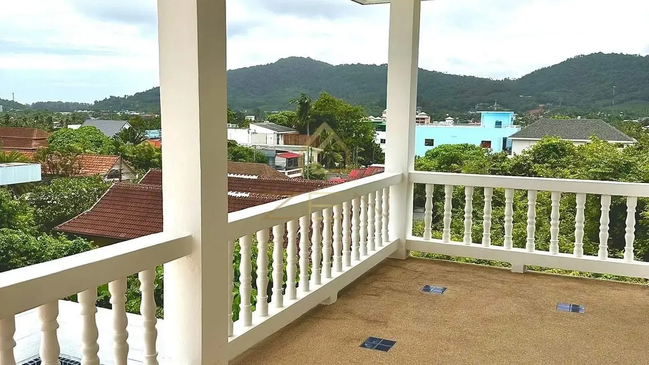 Covered balcony with a white balustrade looking out over rooftops to green hills.