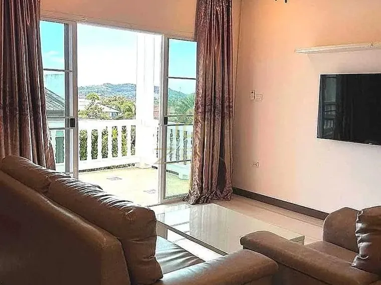 Living room with leather sofas and a glass door to a balcony with a hill view.