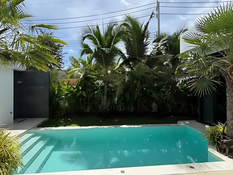 The same villa's pool and garden in daylight, with an outdoor shower and planting along the wall.
