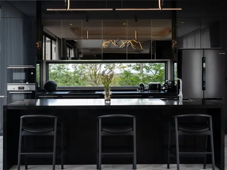 Black island kitchen with bar stools and integrated appliances.